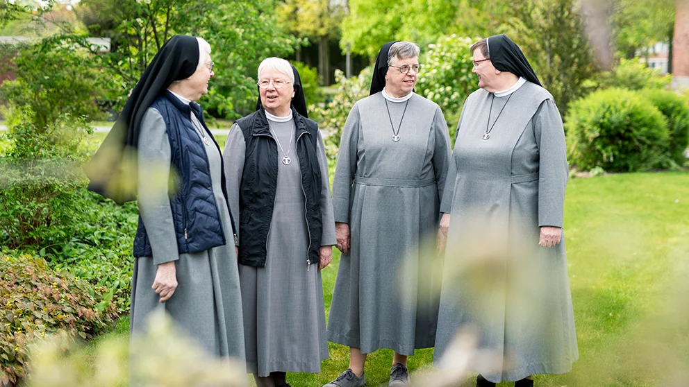 Mehrere ältere Nonnen stehen im Klostergarten nebeneinander und schauen sich an.