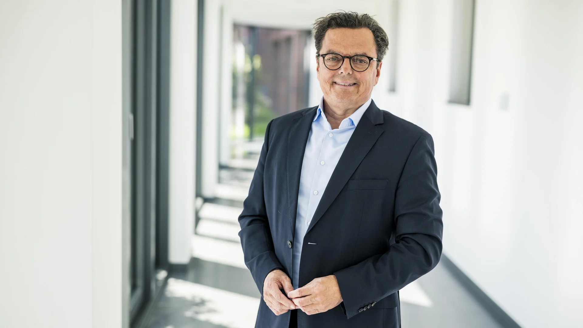 Dr. Ulrich Knopp (Vorstand Medizin) steht auf einem Flur am Fenster und lächelt.
