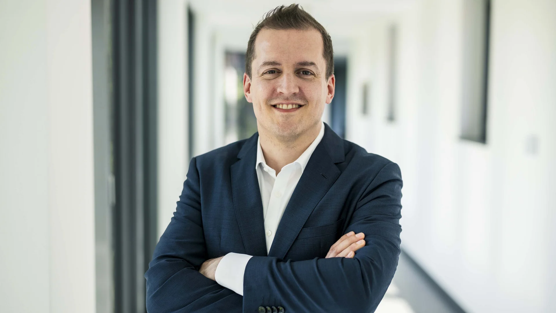 Dr. Christian Frank (Vorstand Finanzen) steht auf einem Flur am Fenster und lächelt.
